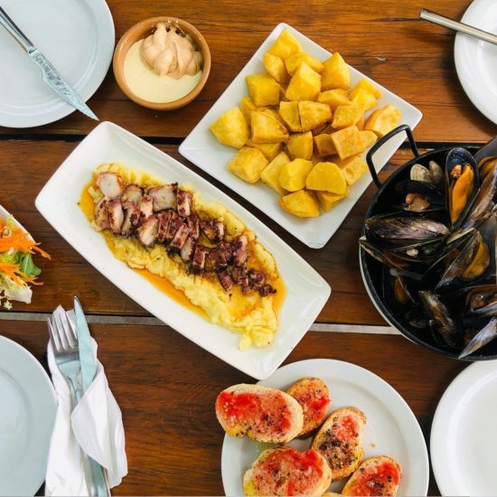 Assorted Barcelona tapas on a wooden table: patatas bravas, mussels, pan con tomate, grilled octopus and aioli.