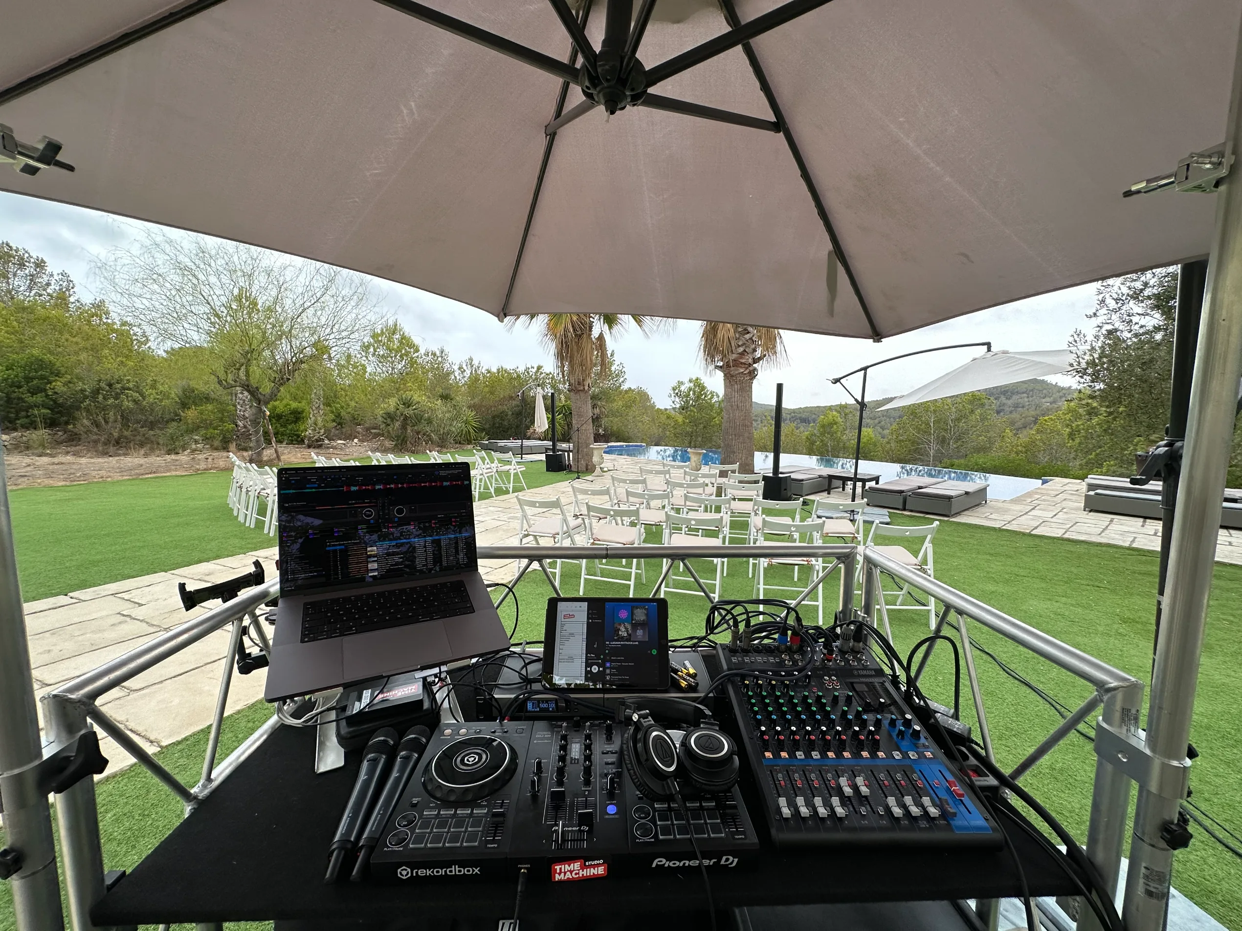Platinas de DJ instaladas junto a filas de sillas blancas para una ceremonia al aire libre
