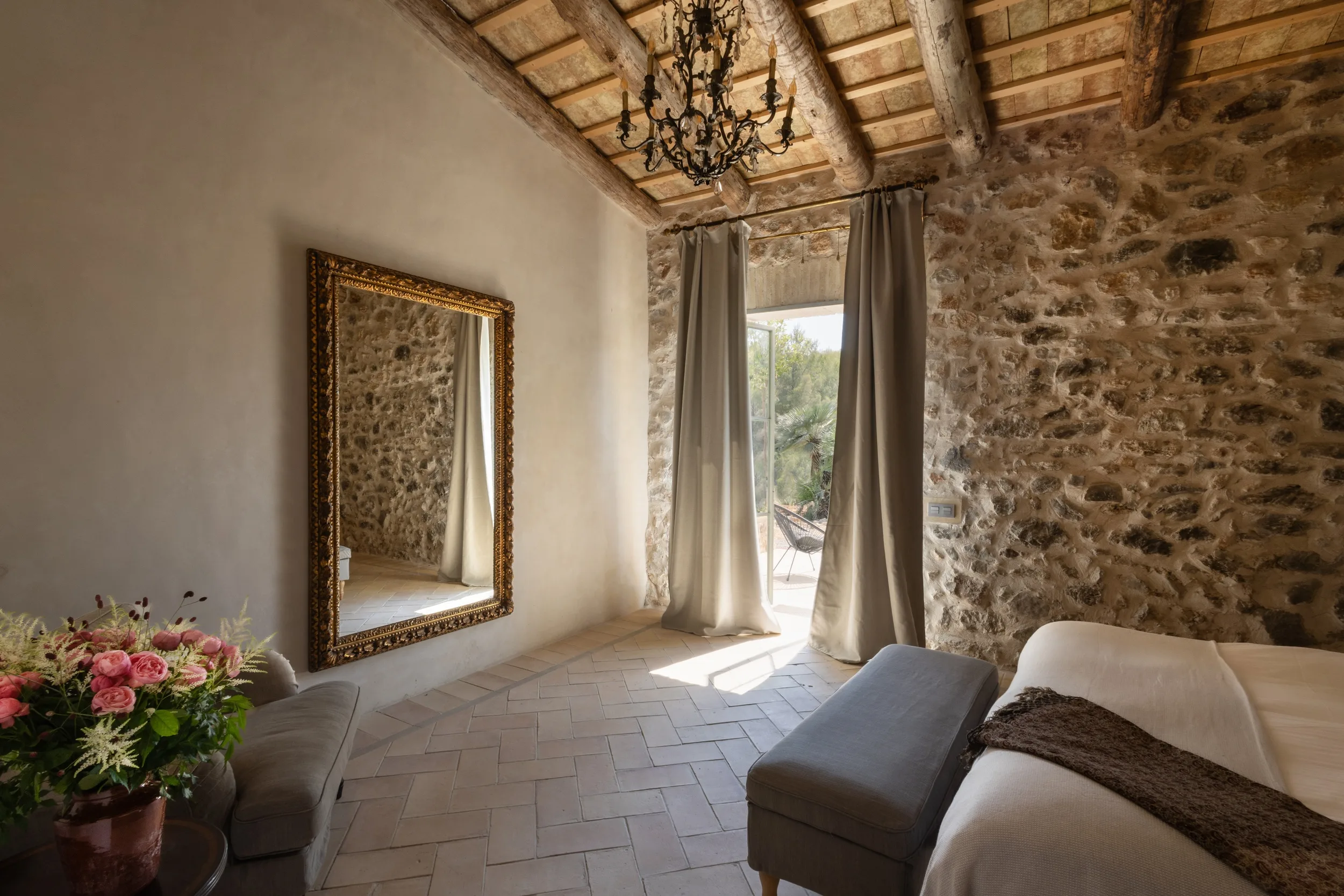 Habitación de invitados con suelo de baldosas en espiga, lámpara de araña y cortinas de lino