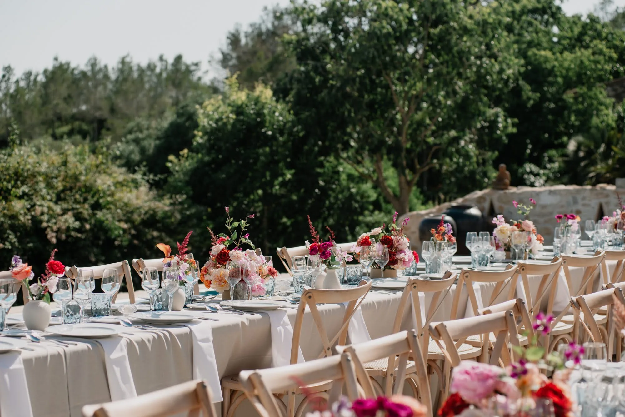 Outdoor wedding table with pink and red florals under the trees at Villa Alcazar del Garraf