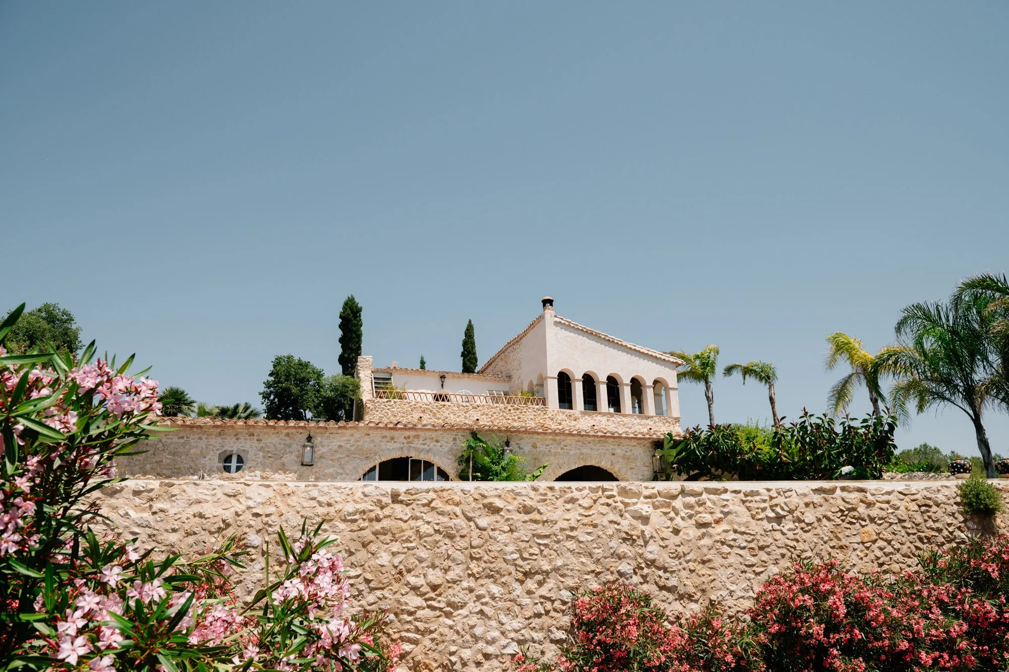 Loggia de pedra d'arcades sobre un mur de jardí florit a la Vila Alcázar del Garraf