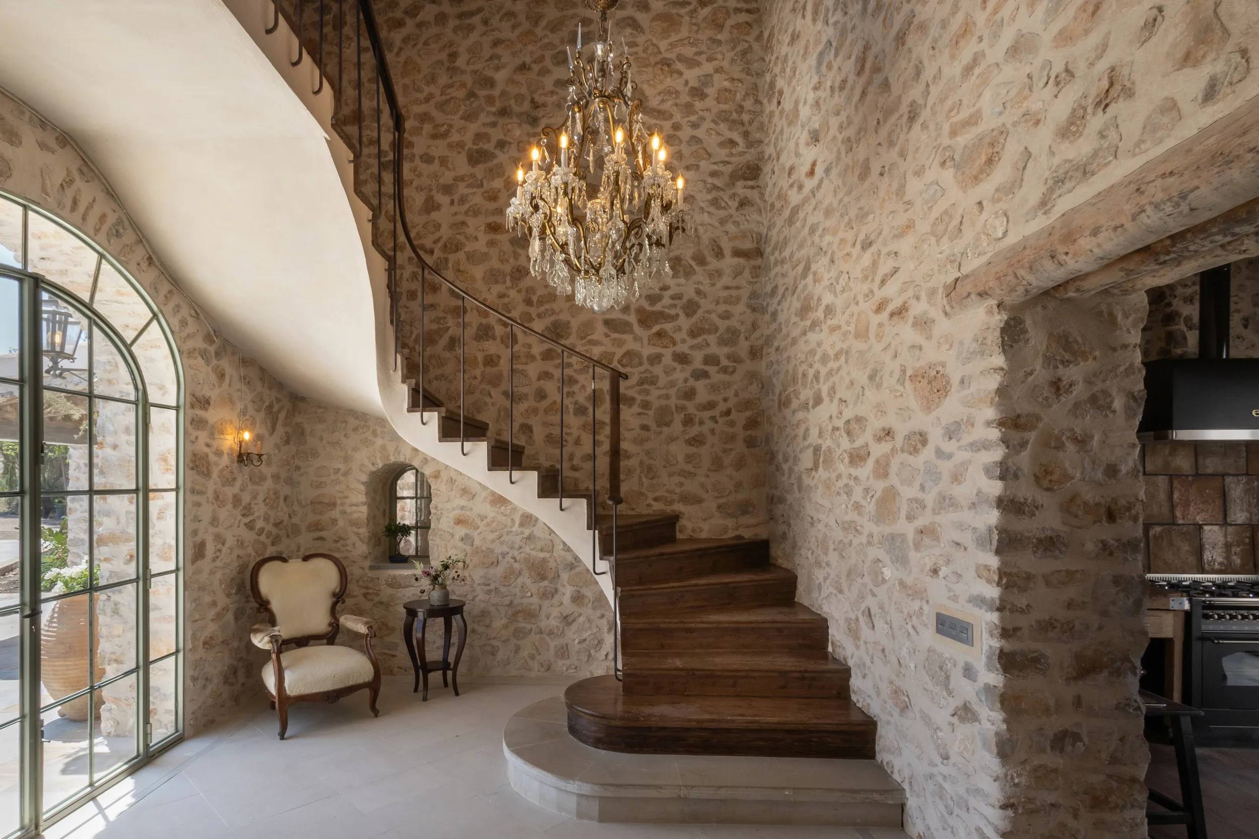 Curved stone staircase and crystal chandelier in the hallway at Mansion Los Naranjos
